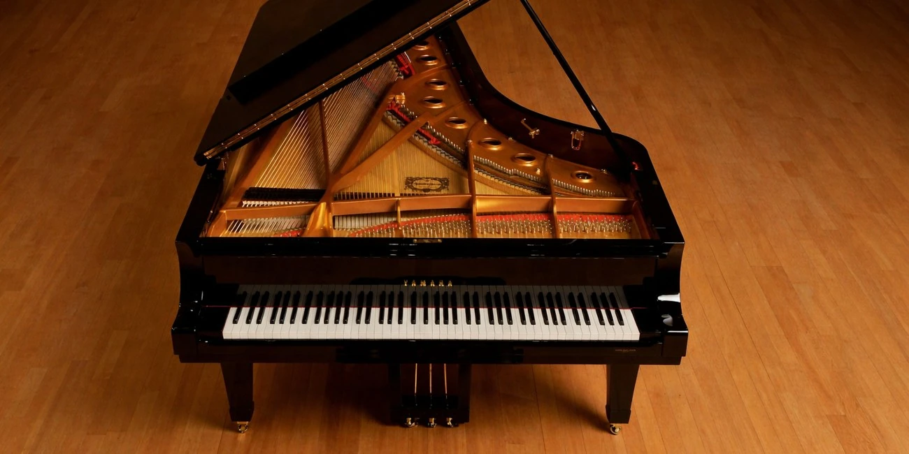 Yamaha grand piano with its lid open on a wooden floor.